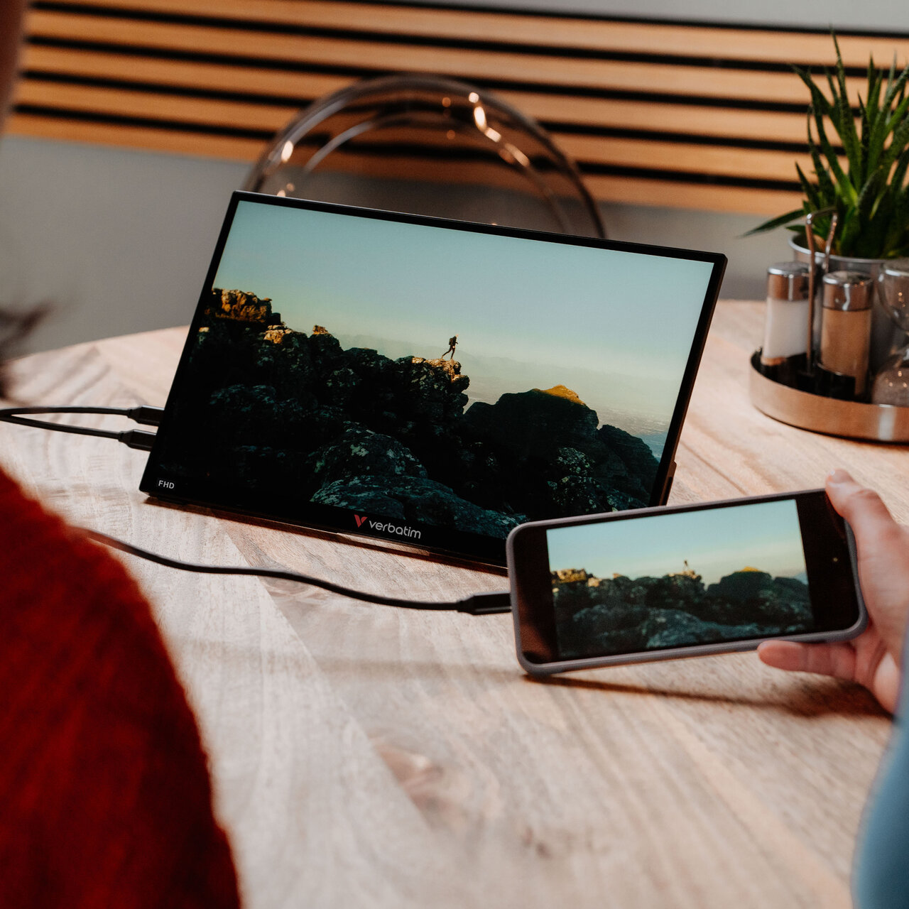 Verbatim 14-inch portable Full HD monitor connected to a smartphone, displaying mirrored content on a wooden table, ideal for mobile entertainment, travel, and productivity on the go